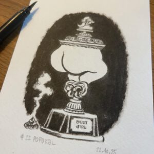 Eine schwarz-weiße Tuschezeichnung einer Trophäe in Form eines Gesäßes mit der Aufschrift "BEST ASS". Aus einem kleinen Gegenstand an der Seite steigt Rauch auf. Im Hintergrund sind ein Füllfederhalter und eine Holzfläche zu sehen. Die Zeichnung ist mit 22.10.25 datiert.